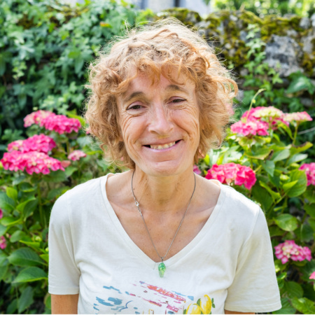 Femme souriante devant des hortensias roses, jardin verdoyant.